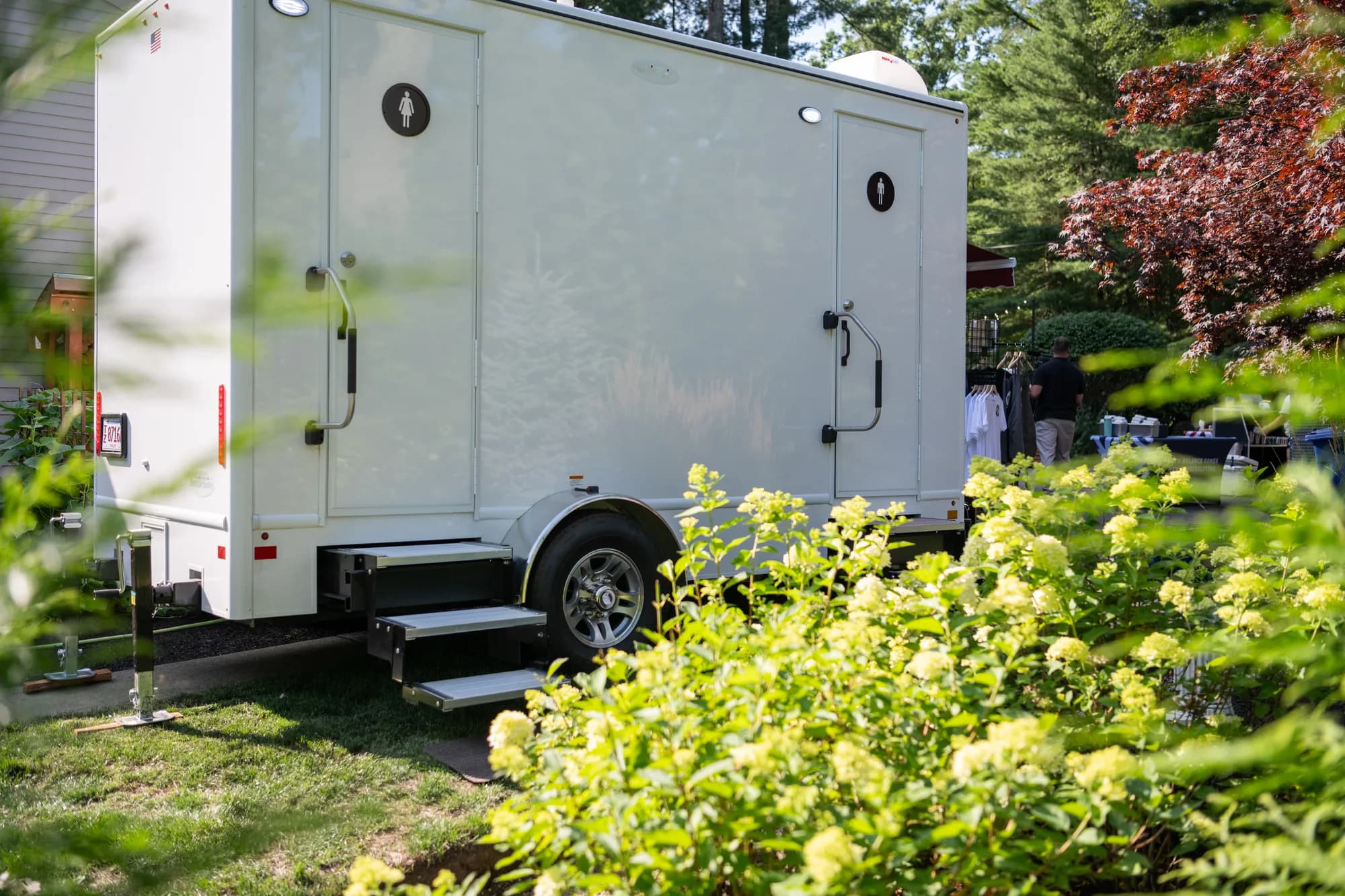 White luxury mobile restroom trailer set up beside blooming hydrangeas at an outdoor New England wedding