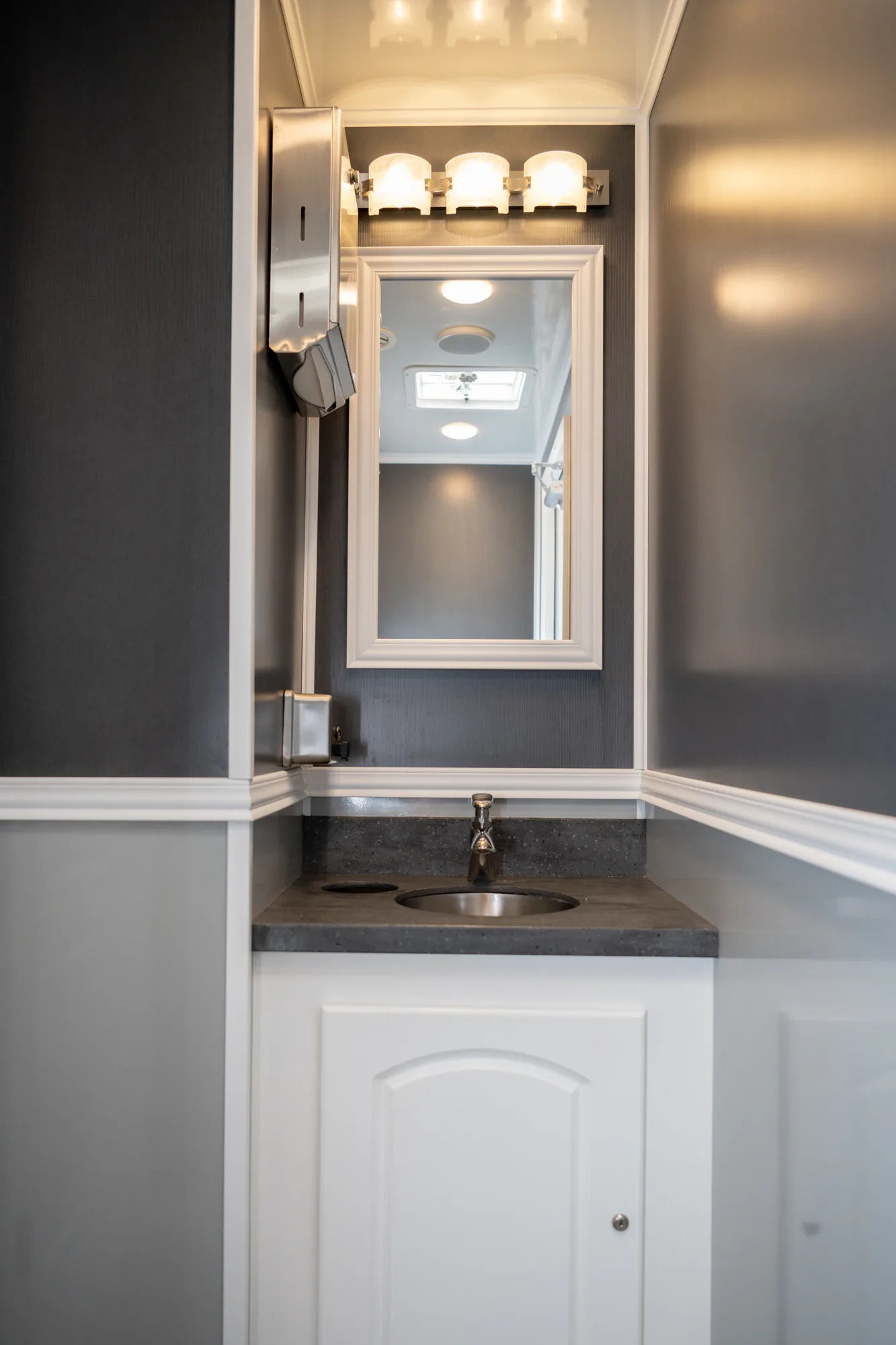 Interior vanity of a luxury restroom trailer with framed mirror, stone countertop, and soft vanity lighting